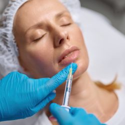 Beautician hand in sterile gloves over female client face. Anti-aging injection and plastic surgery in modern beauty clinic. Closeup view